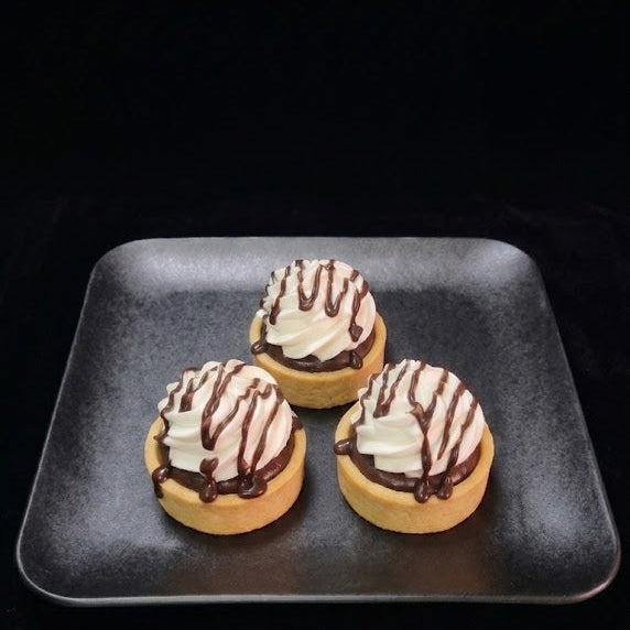 Mini chocolate cream tartlets filled with rich chocolate cream and topped with non dairy whip, and chocolate ganache drizzle n a buttery pastry shell.