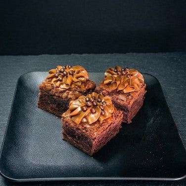 Three brownies with espresso coffee fudge frosting on a black plate against a dark background from the best bakery in the las vegas