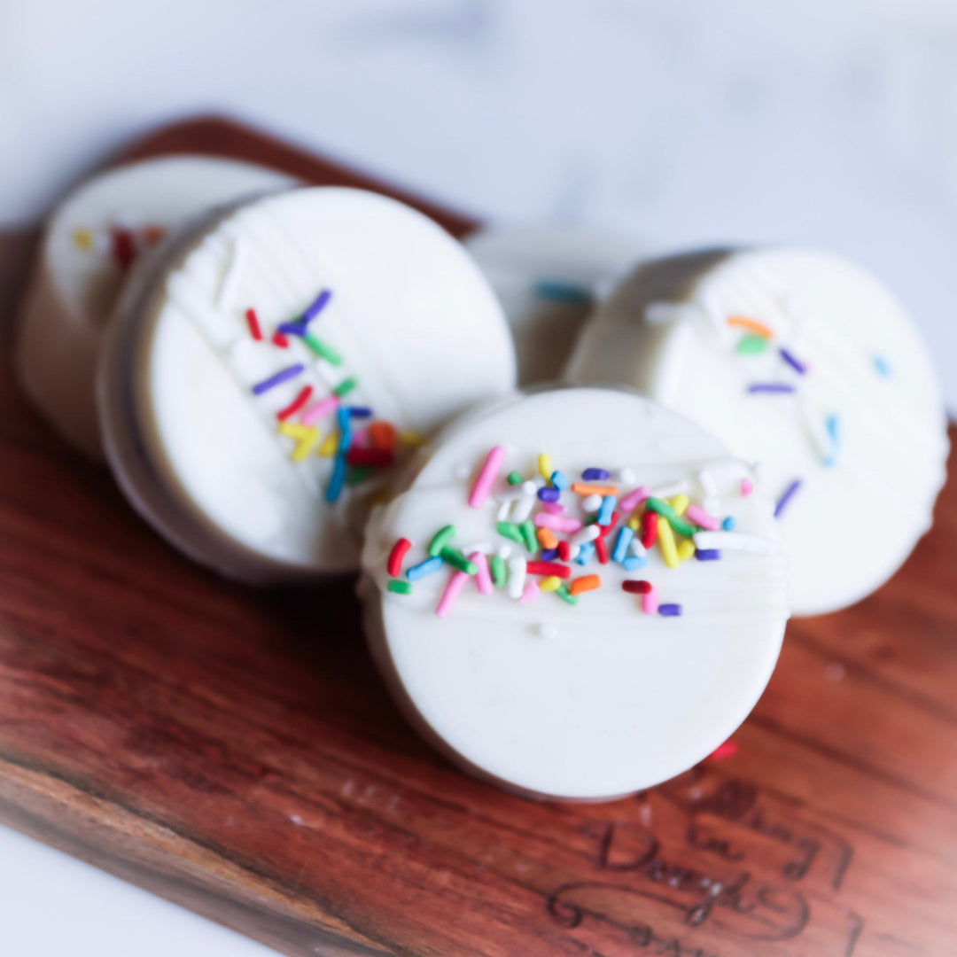 Three white oreos with colorful sprinkles on a wooden surface