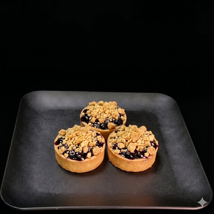 Three small pies with crumb topping on a dark tray against a black background