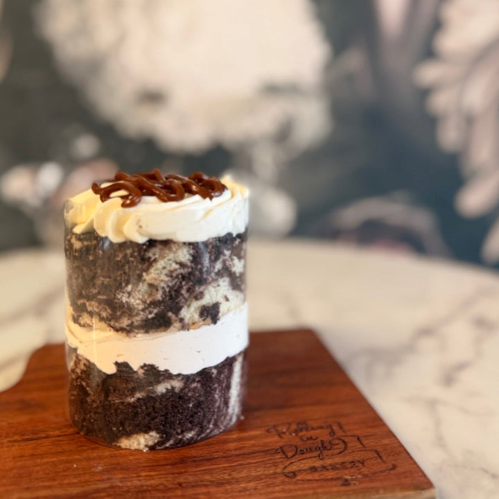 Layered dessert on a wooden board with a blurred floral background, Marble Cake with caramel mousse