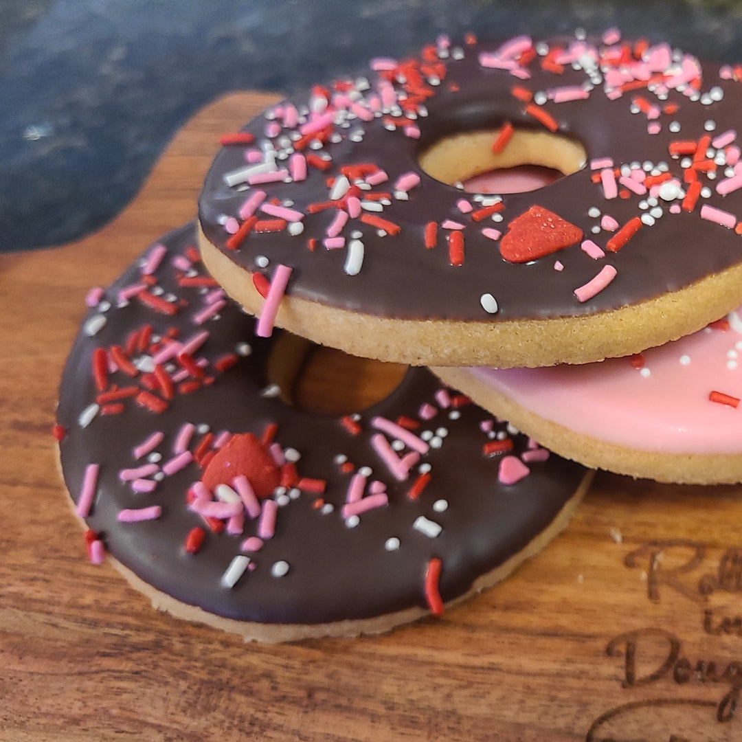 Decorative cookies with pink and red sprinkles on a wooden board with 'Rolling in Dough' branding.