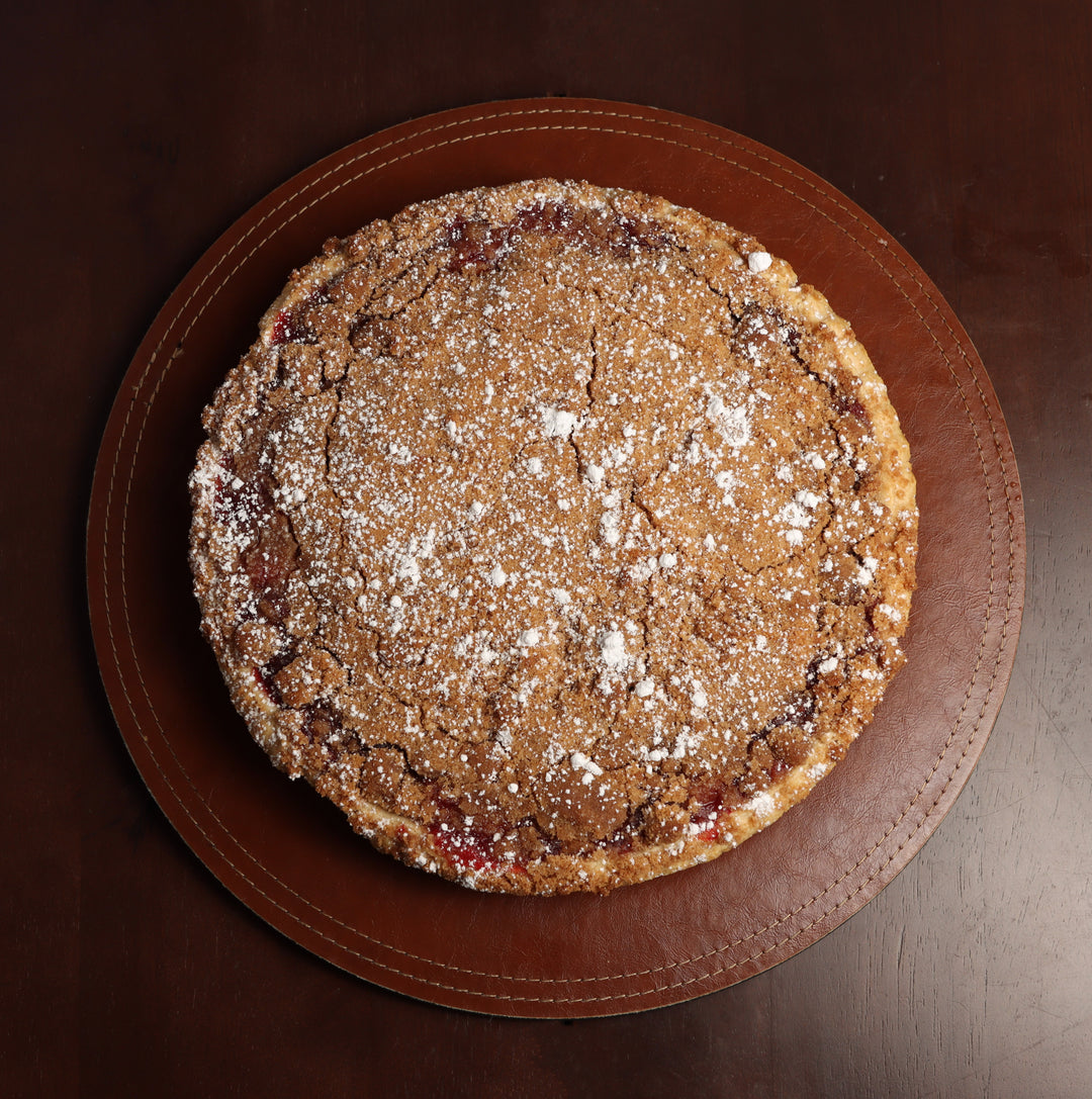 A whole strawberry rhubarb pie dusted with powdered sugar on a brown plate.