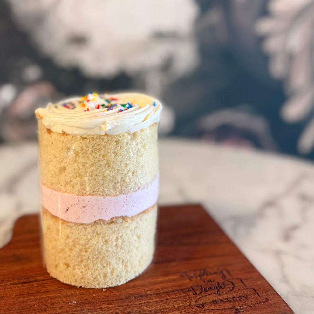 Small cylindrical cake with colorful decorations on a wooden board against a blurred background, Vanilla cake with Raspberry mousse