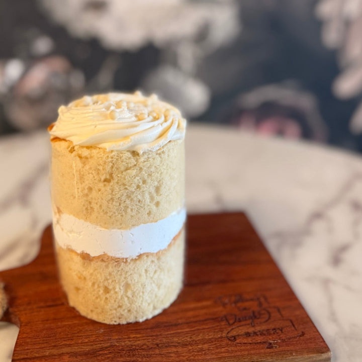 Small cylindrical cake with white frosting on a wooden board with a blurred background, vanilla cake with bavarian creme