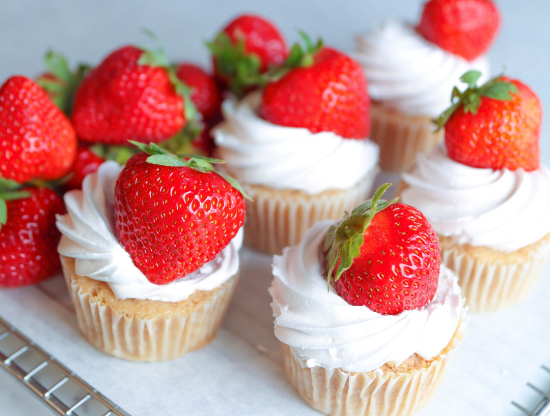Cupcakes with white frosting and strawberries on a white surface
