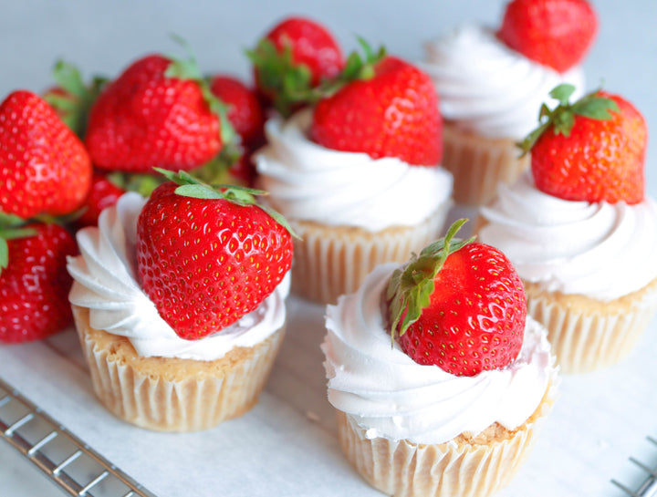 Cupcakes with white frosting and strawberries on a white surface