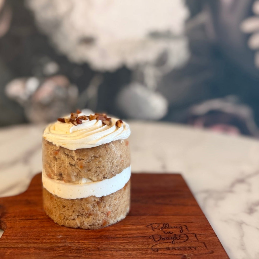 Small layered cake with white frosting on a wooden board against a blurred floral background, carrot cake with cream cheese