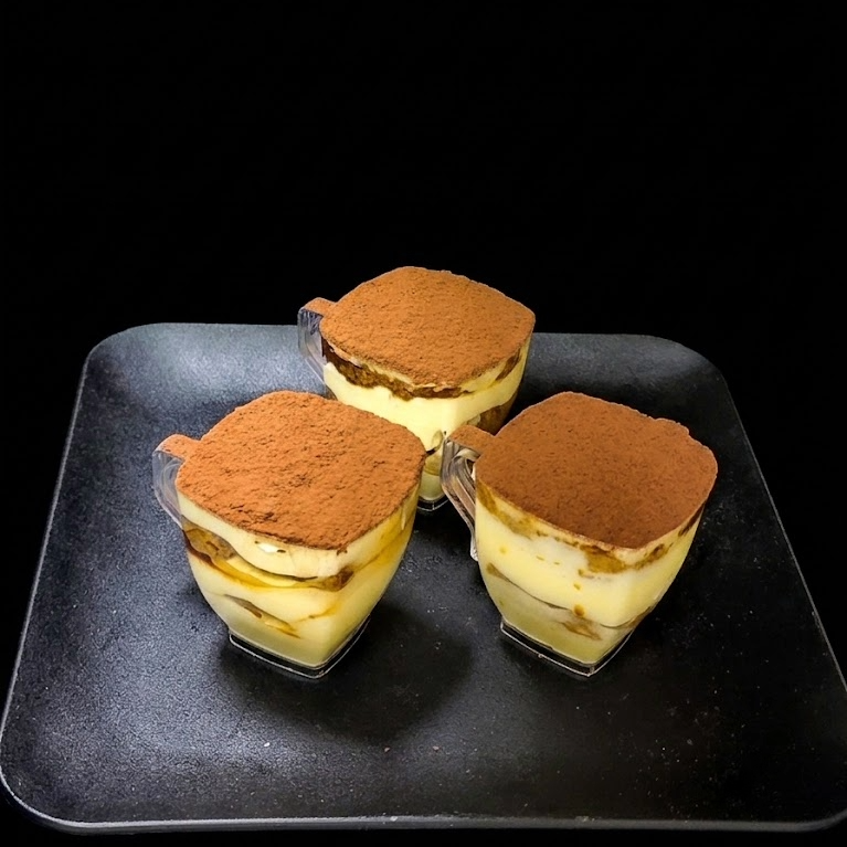 Individual tiramisu dessert with layers of espresso-soaked ladyfingers, mascarpone cream, and cocoa powder topping.