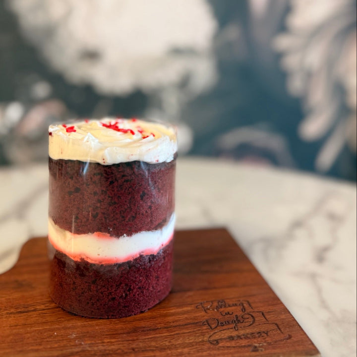 Small red velvet cake with cream cheese frosting on a wooden board against a blurred background